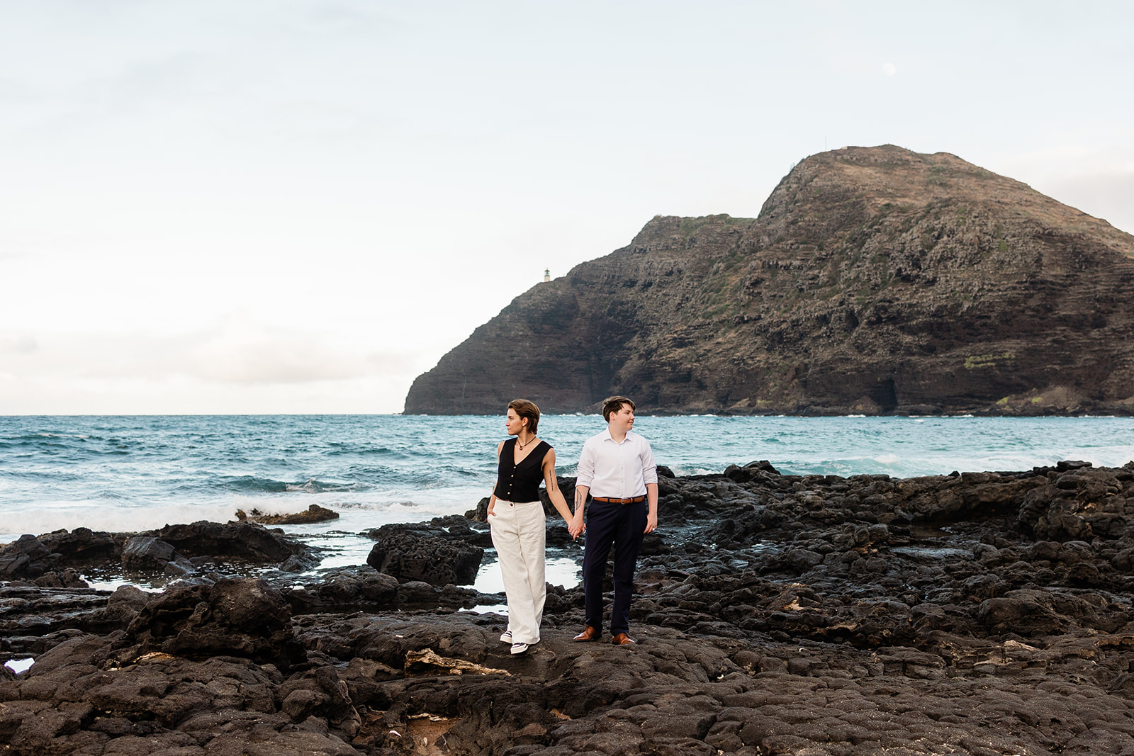 Queer couple holding hands on a black rock beach during their LGBTQ+ friendly elopement in Hawaii