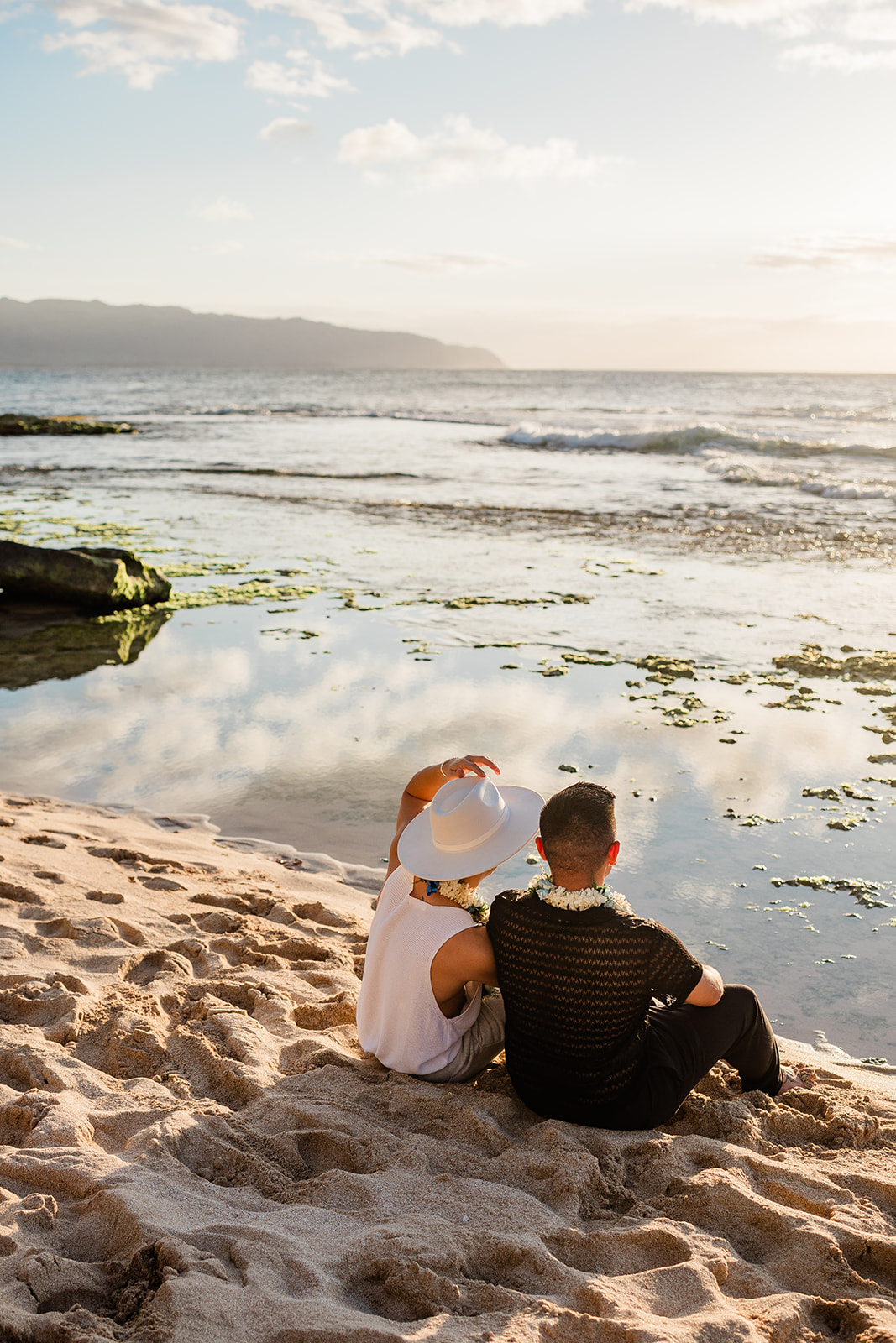 Gay couple seated together looking into the sunset during their Oahu wedding.